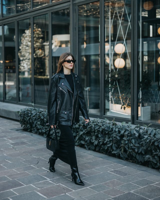 woman wearing leather moto jacket and a midi length dress in black walking down the street